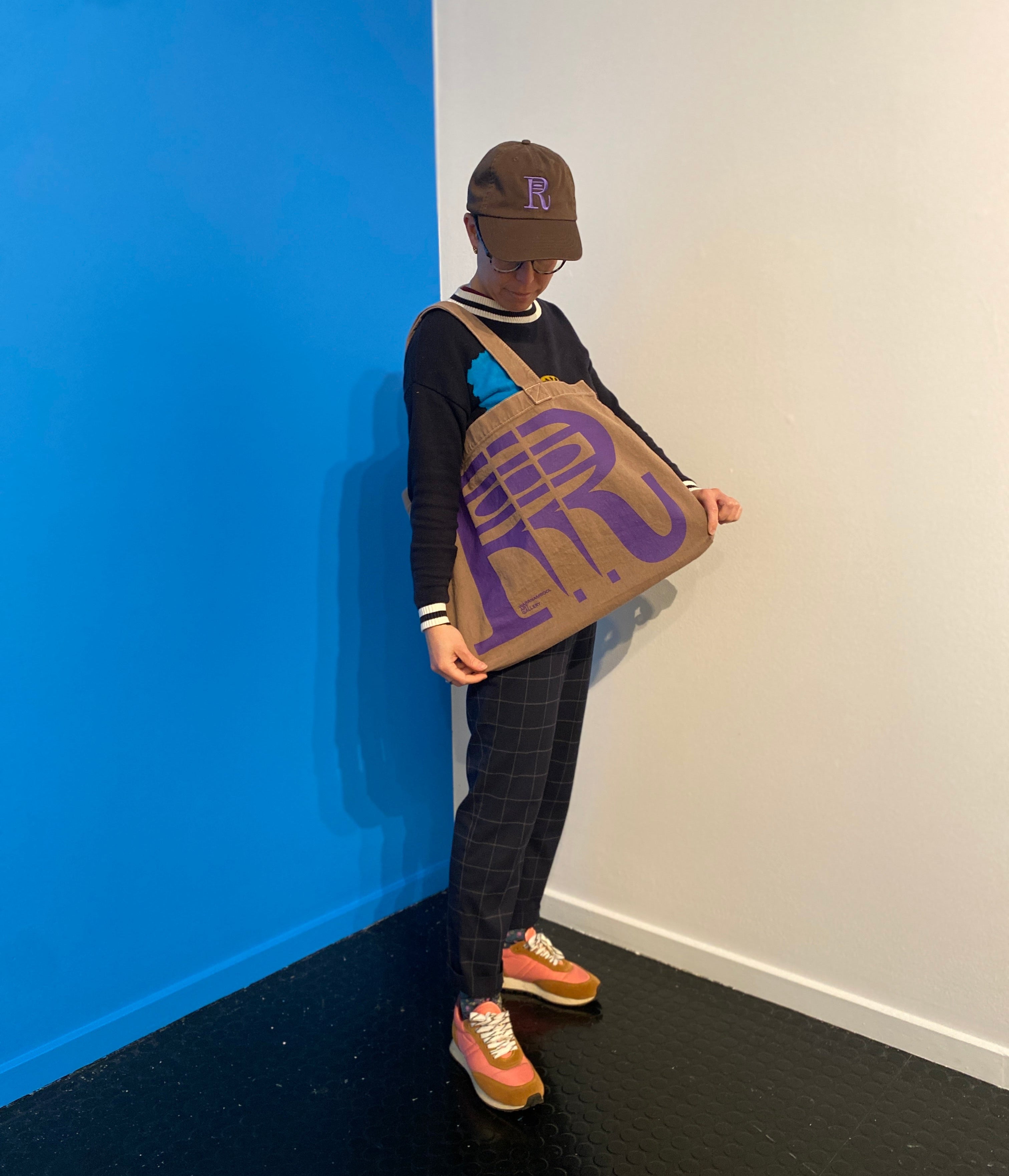 Person holding a large brown bag with a logo against a blue and white wall.